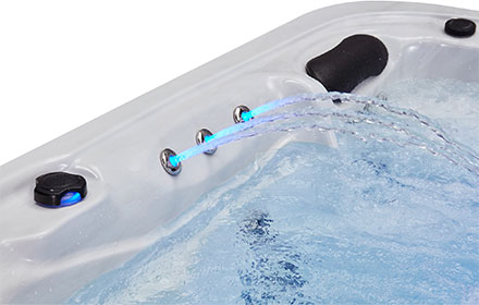 Stainless steel mini-waterfall jets with cyan LED lighting spraying into the tub near a headrest